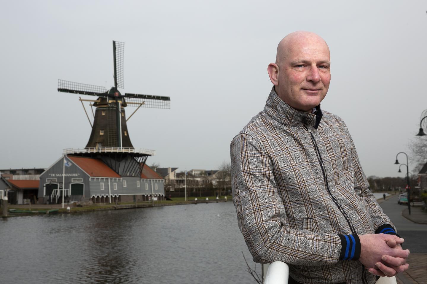 Een foto van Michel de Winter, met op de achtergrond een molen. De foto is gemaakt voor een artikel in de serie RvIG'er in beeld