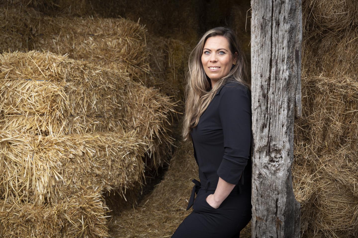 Een foto van Marlies Laarman in een manege met strobalen op de achtergrond. De foto is gemaakt voor een artikel in de serie RvIG'er in beeld