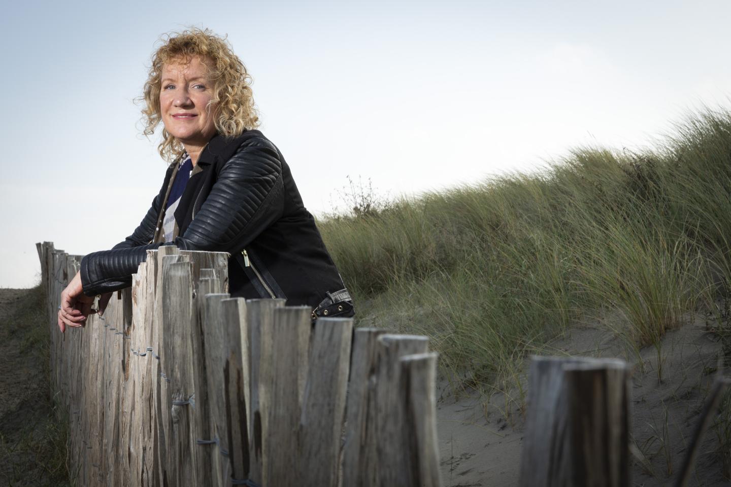 Een foto van Monique van der Veer, met duinen op de achtergrond. Deze foto is gebruikt voor een artikel in de serie RvIG'er in beeld